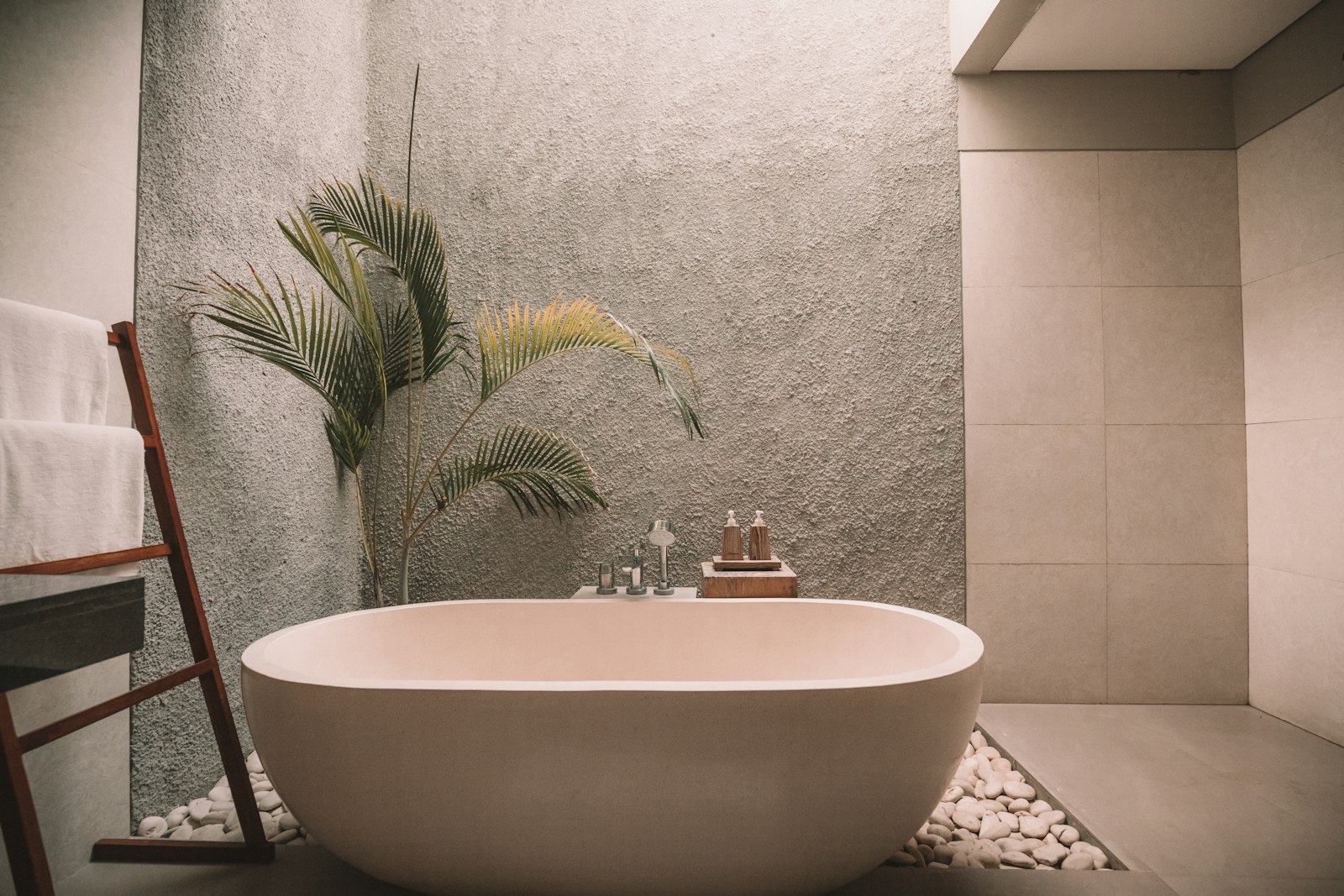 Stone soaking tub on white pebbles beside a palm